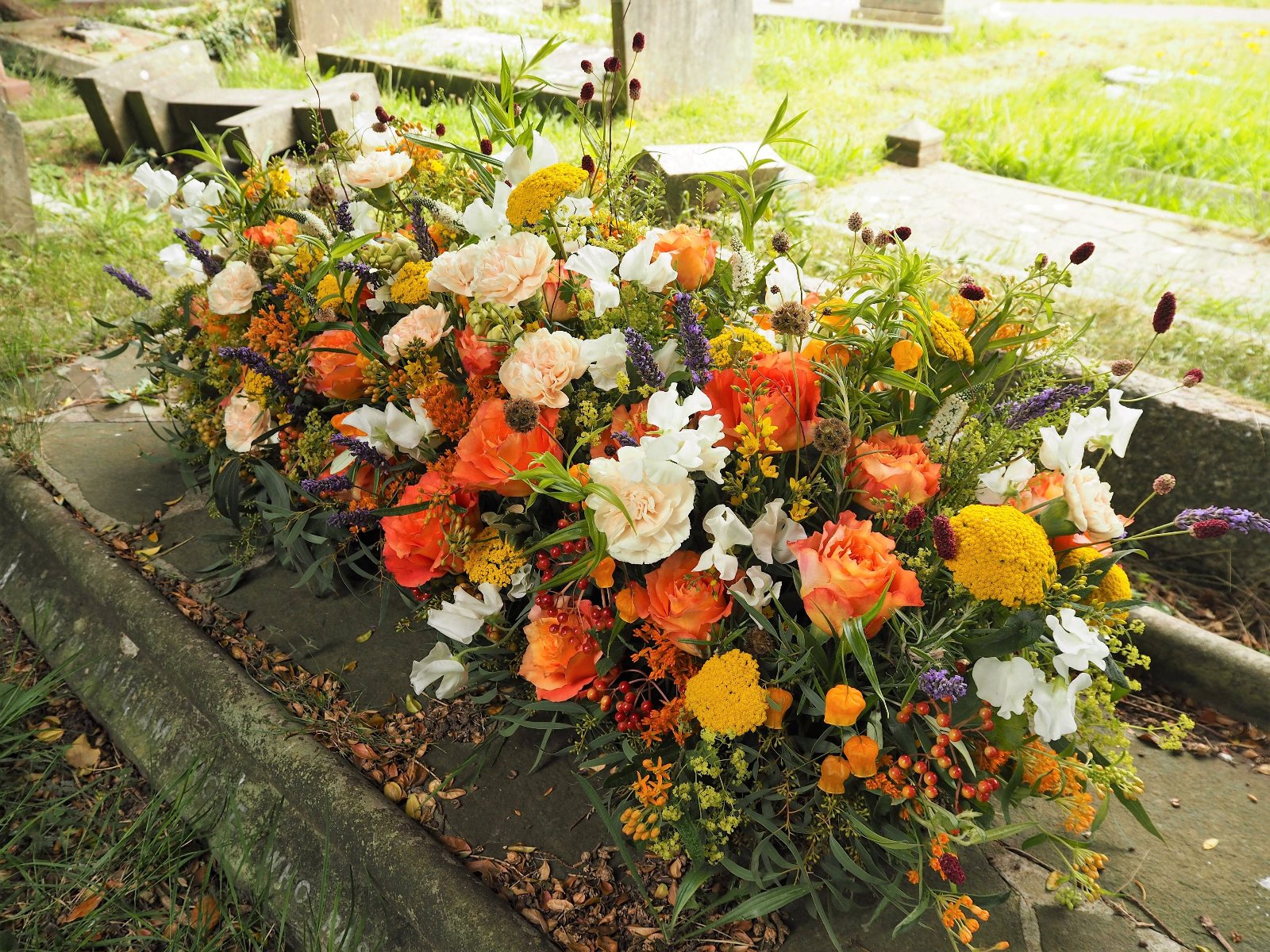 A Casket Spray full o warm sunset colours, placed on a grave